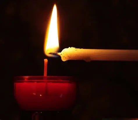 White candle lighting red votive candle in dark setting, close-up flame