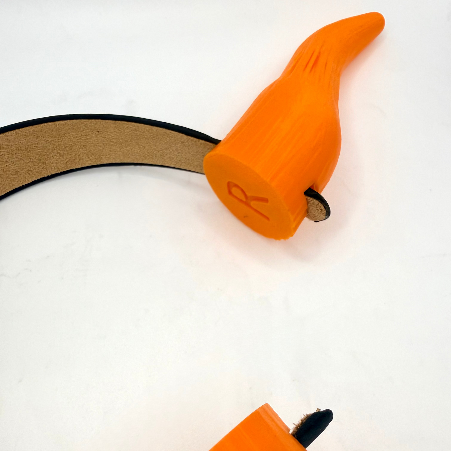 Close-up of bright orange over-ear horns on a white background, showing the right horn with a small 'R' mark, the left horn at the bottom, and a black headband.